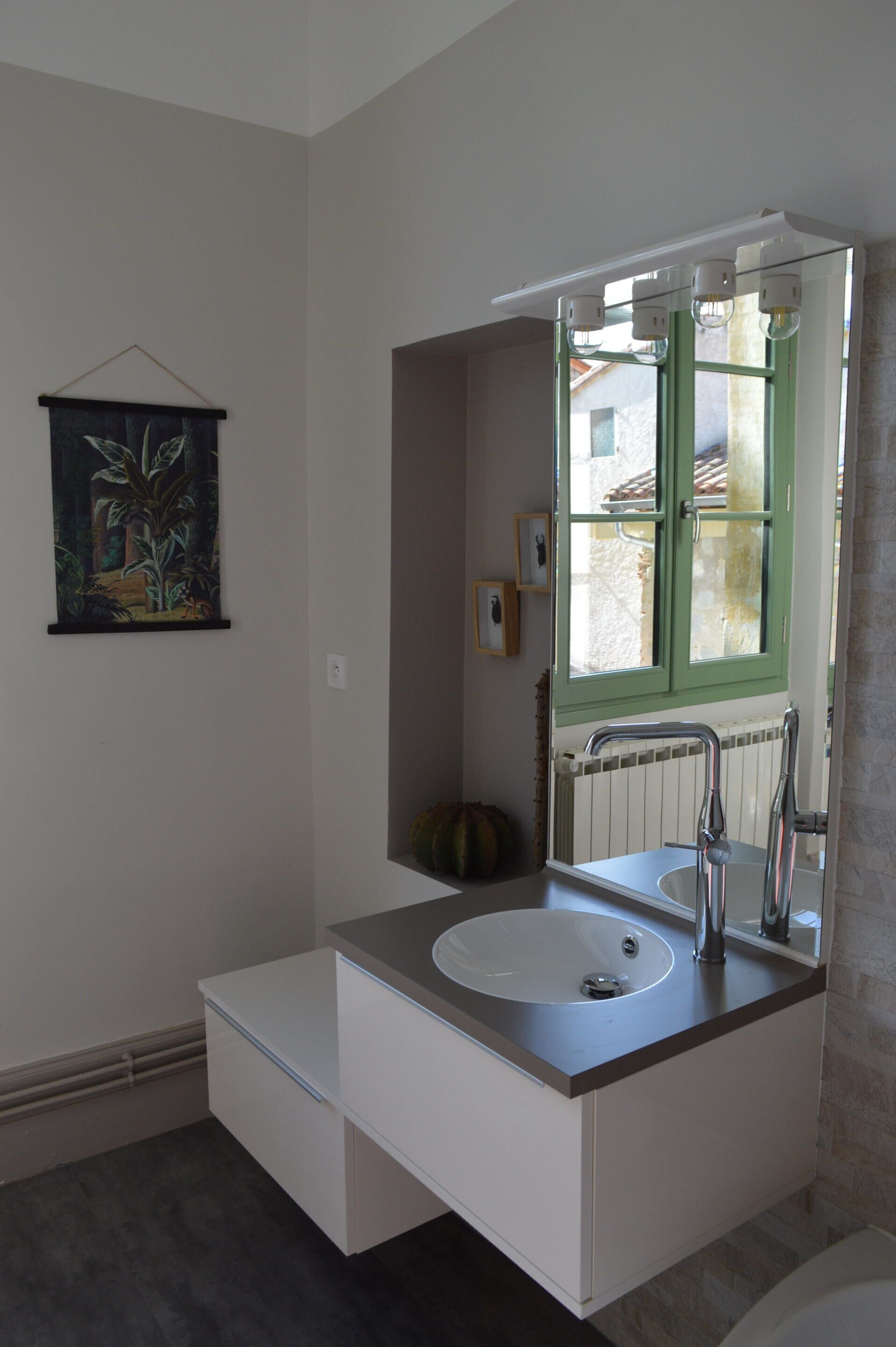Een badkamer met een wit wastafelmeubel, een spiegel en een raam met groene luiken.