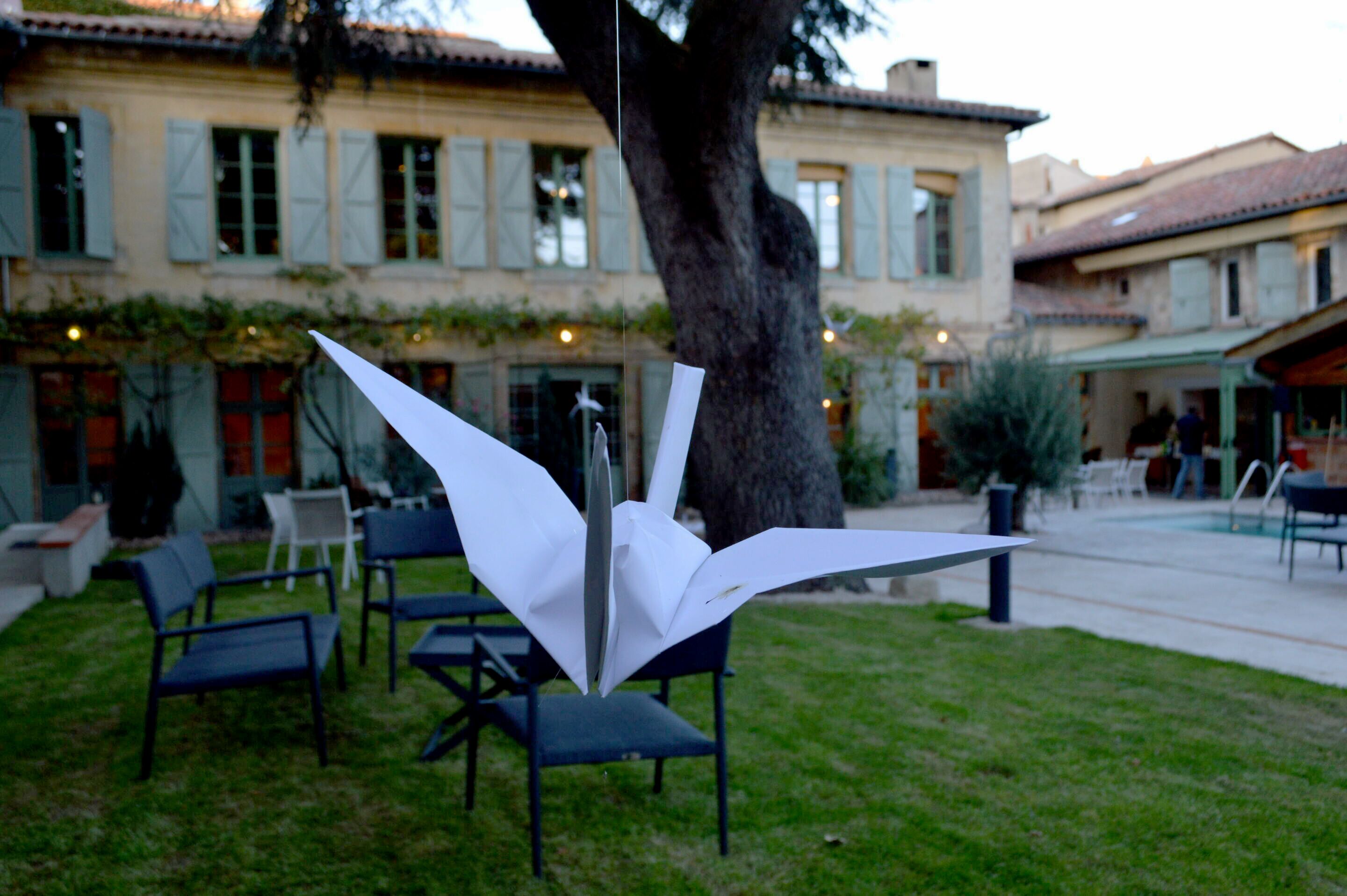 A courtyard with outdoor seating, a large tree, and a building with shutters in the background.