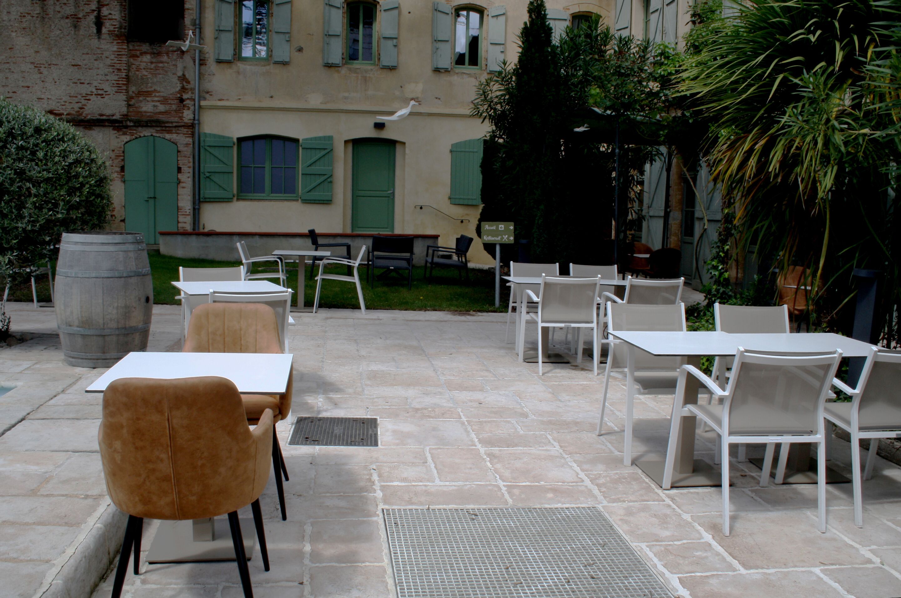 An outdoor patio with white tables and chairs, a green door, and a building with shutters in the background.