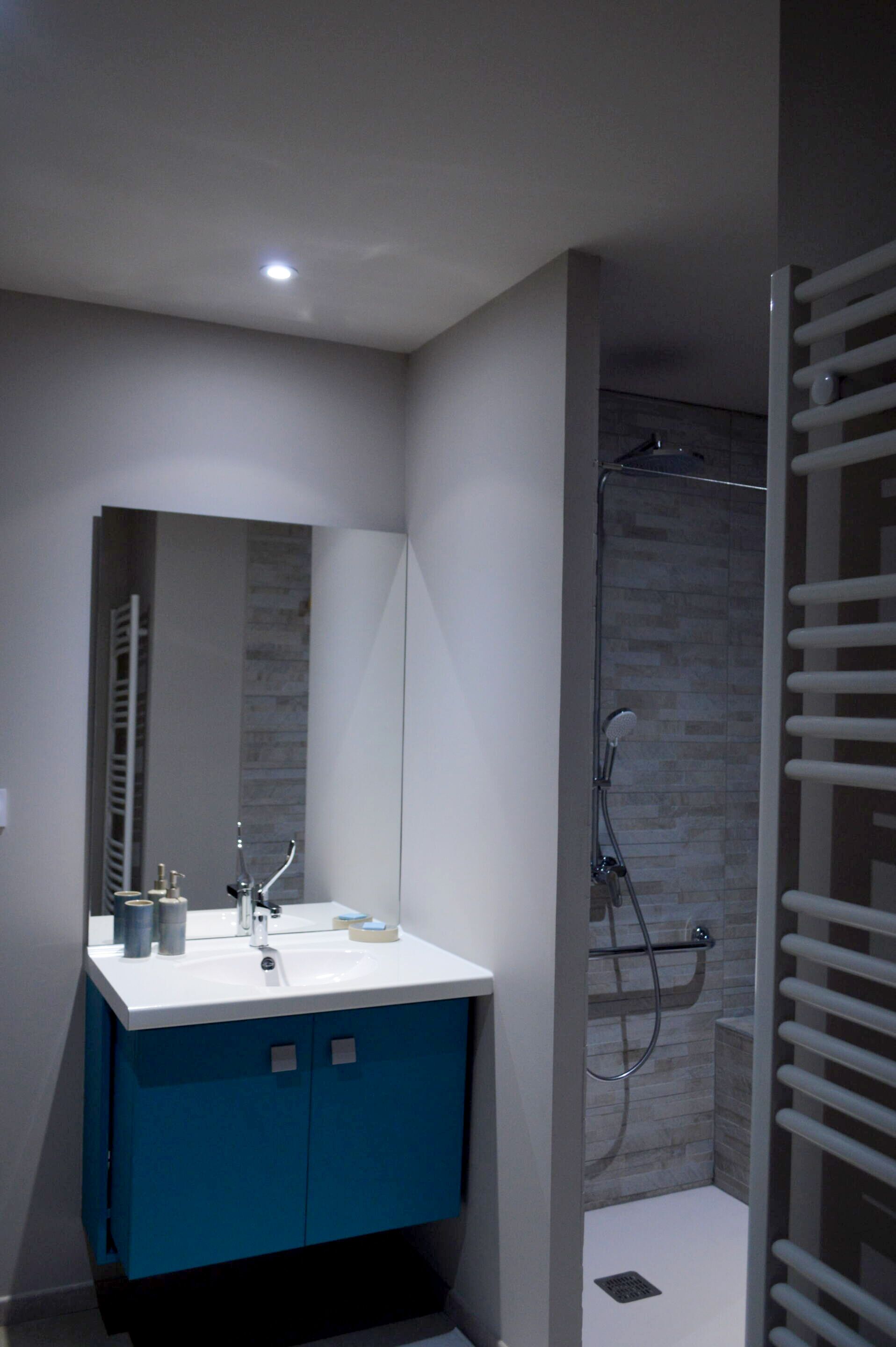 A modern bathroom with a blue vanity, a mirror, and a shower area.