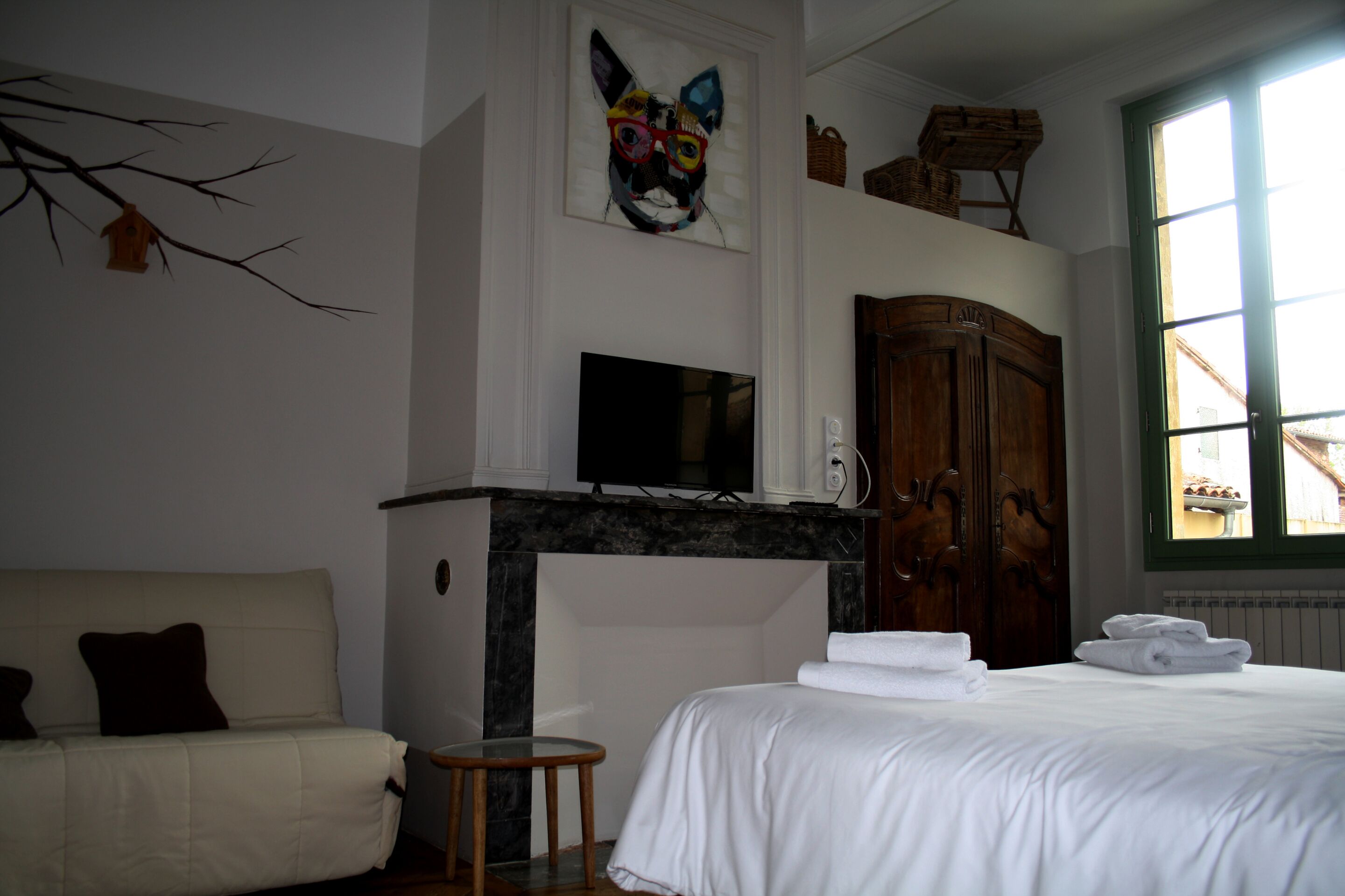 A hotel room with a bed, a TV, a fireplace, a wooden wardrobe, and a window with a view.