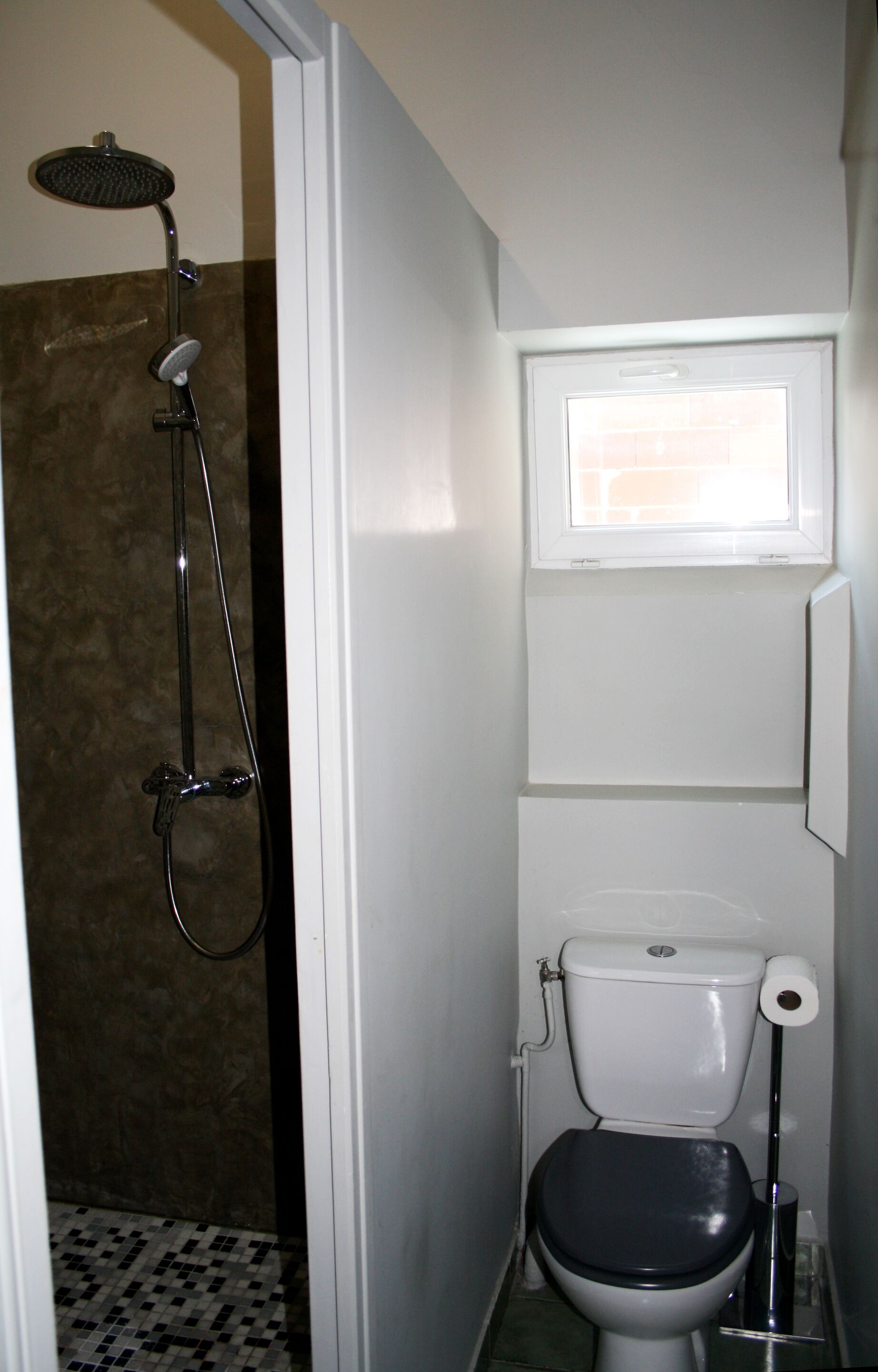 A bathroom with a shower, toilet, and a small window above the toilet.
