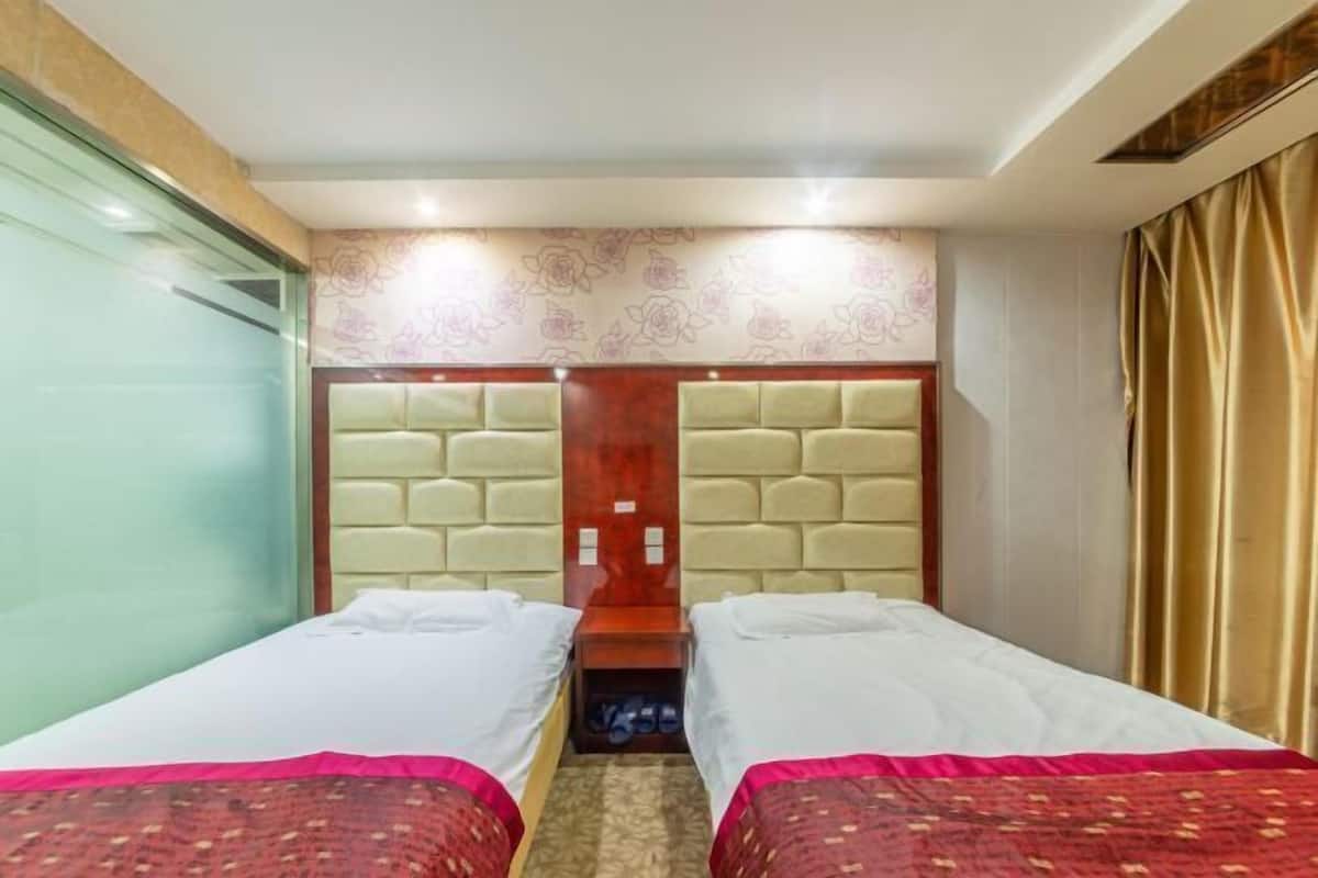 Camera d'albergo con due letti, una testiera in legno, una parete decorata e una finestra con tende.