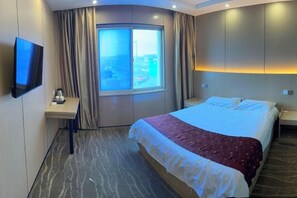 A hotel room with a bed, a TV, a window with curtains, a bedside table, and a view of the city. - Ningtai Business Hotel (Shanghai)