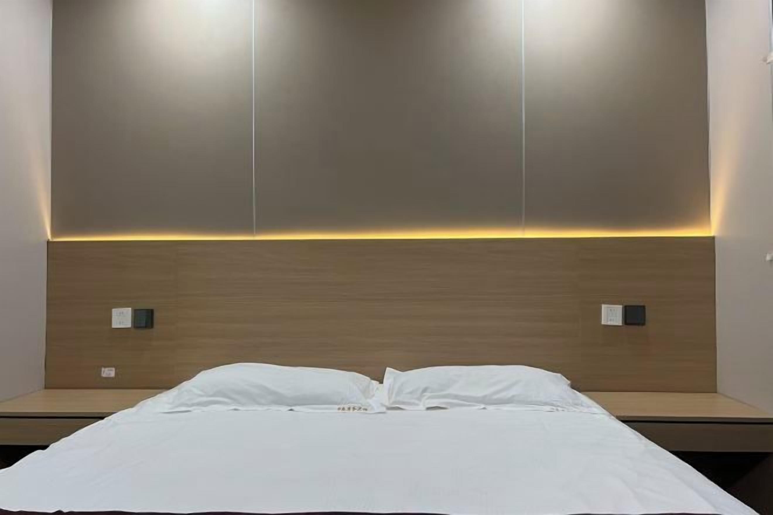 Habitación de hotel con cama, cabecera de madera y dos interruptores de luz en la pared.