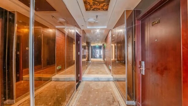 Un couloir d’hôtel aux murs recouverts de miroirs, avec un tapis à motifs et une porte en bois sur la droite.