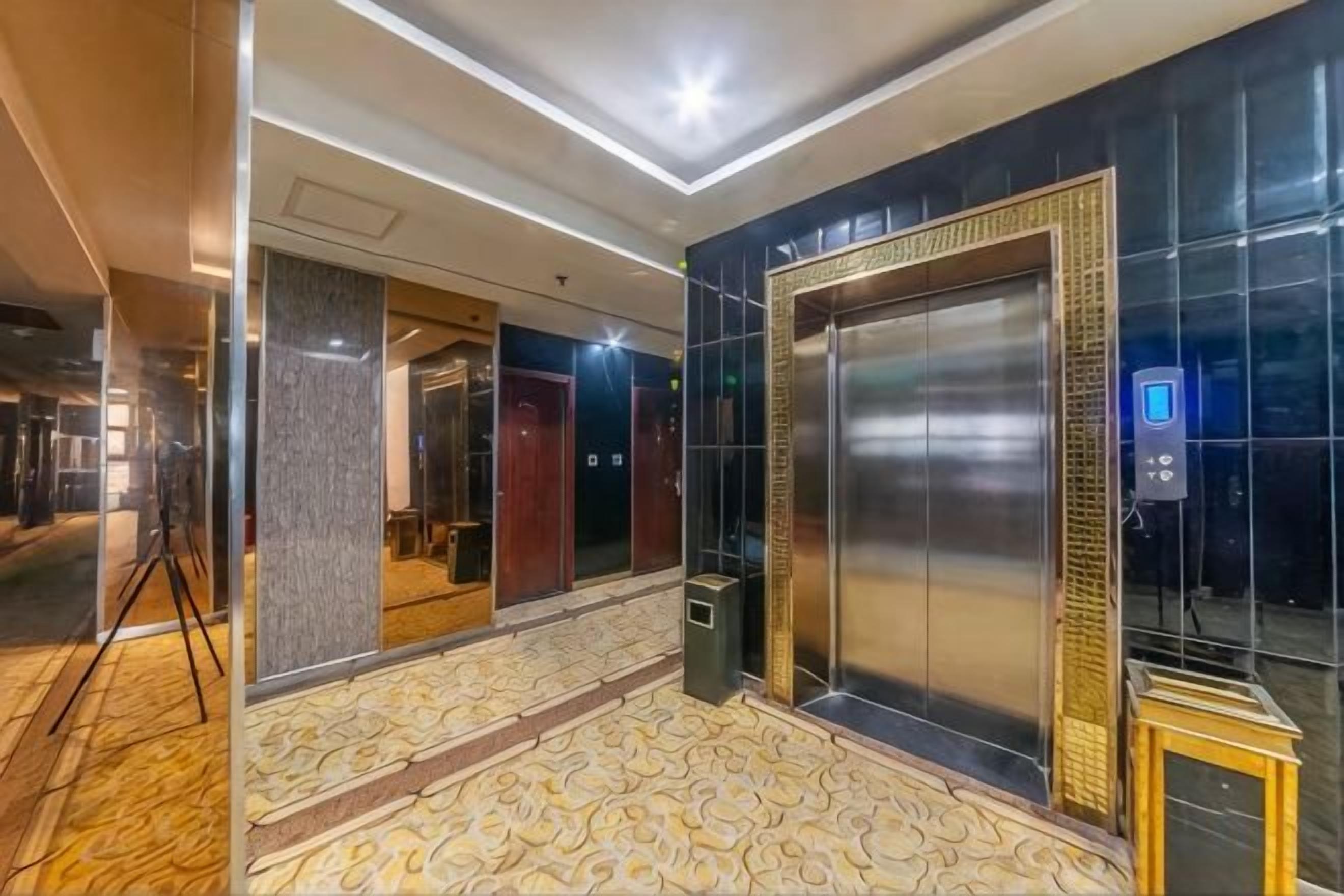A hotel lobby with a patterned floor, a large elevator, and a modern light fixture.