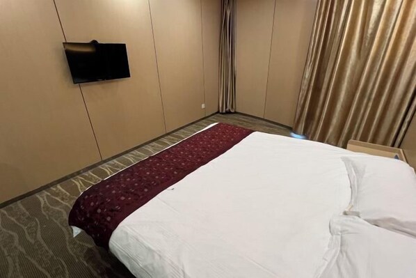 Ett hotellrum med en säng, en platt-TV som är monterad på väggen, ett mönstrat golv och ett fönster med gardiner.