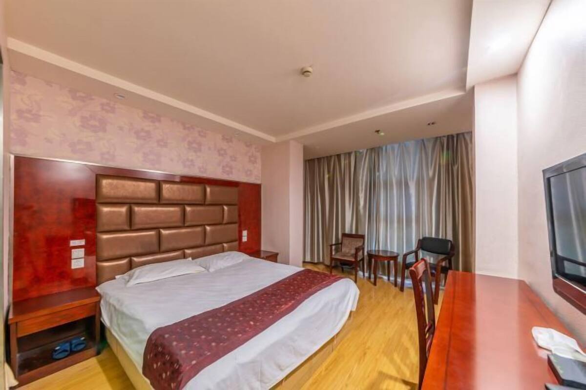 Una camera d'albergo con un letto grande, una testiera in legno, una TV, una scrivania e una sedia.