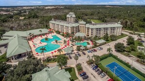 Un grand hôtel doté d’une piscine centrale, de nombreuses chambres et d’un court de tennis.