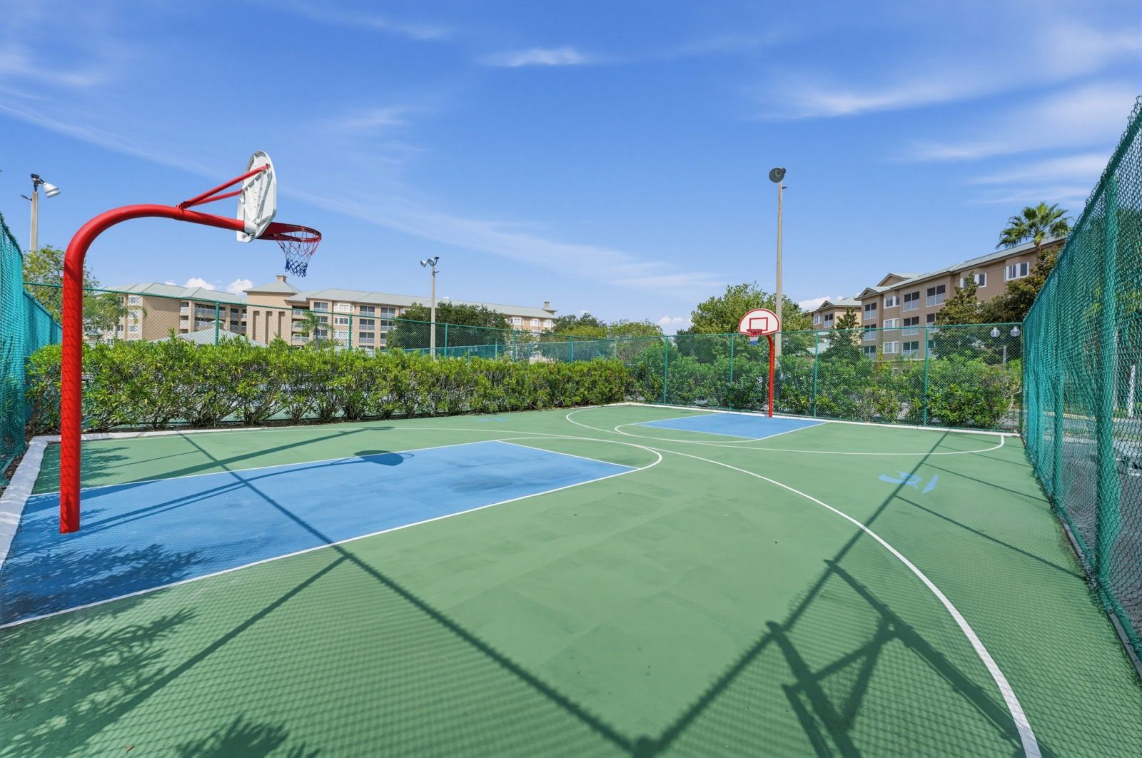 Ein Basketballplatz im Freien mit zwei Körben, umgeben von einem grünen Zaun und Bäumen.