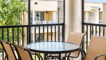 Een balkon met een ronde tafel en stoelen, een plafondventilator en uitzicht op omliggende gebouwen.
