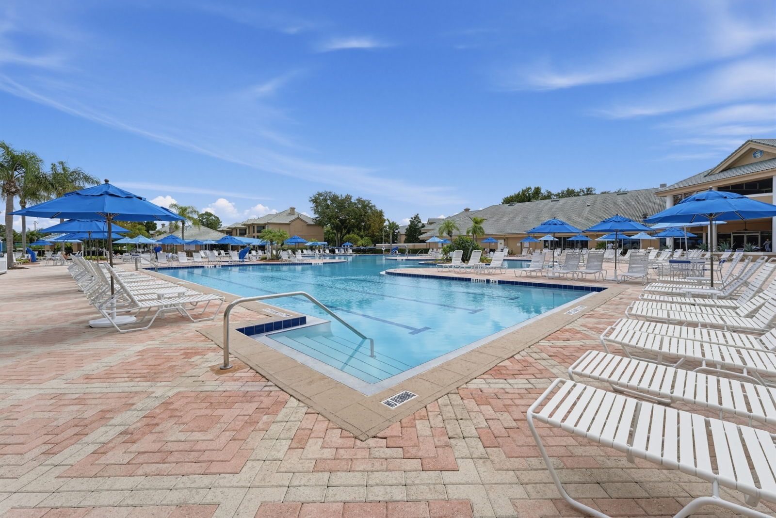 Expansive pool with blue umbrellas, lounge chairs, and open skies