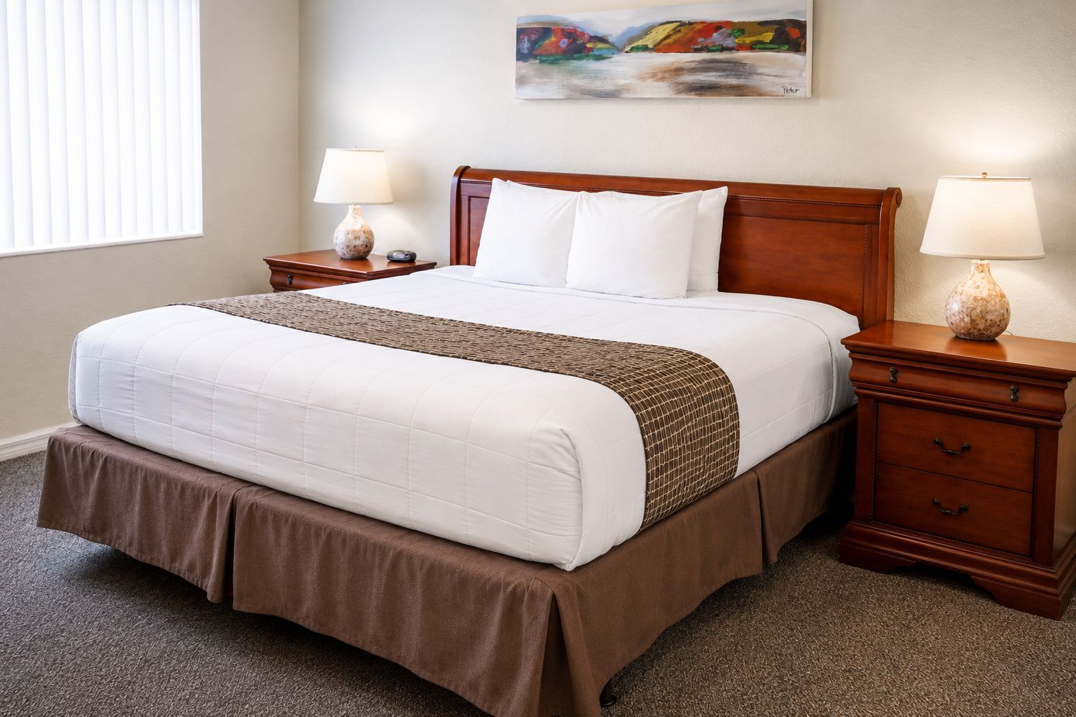 Una habitación de hotel con una cama grande, dos mesitas de noche con lámparas, un cuadro en la pared y suelo cubierto de alfombra.