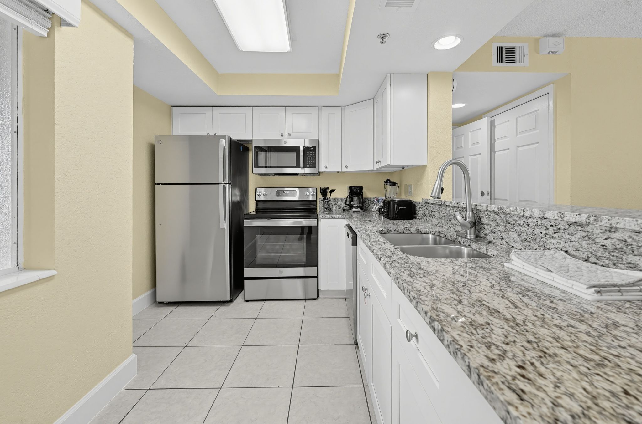 A modern kitchen with stainless steel appliances, white cabinetry, and a granite countertop.