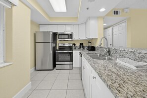 A modern kitchen with stainless steel appliances, white cabinetry, and a granite countertop. - Spacious 2BR Villa Near Disney (Kissimmee)
