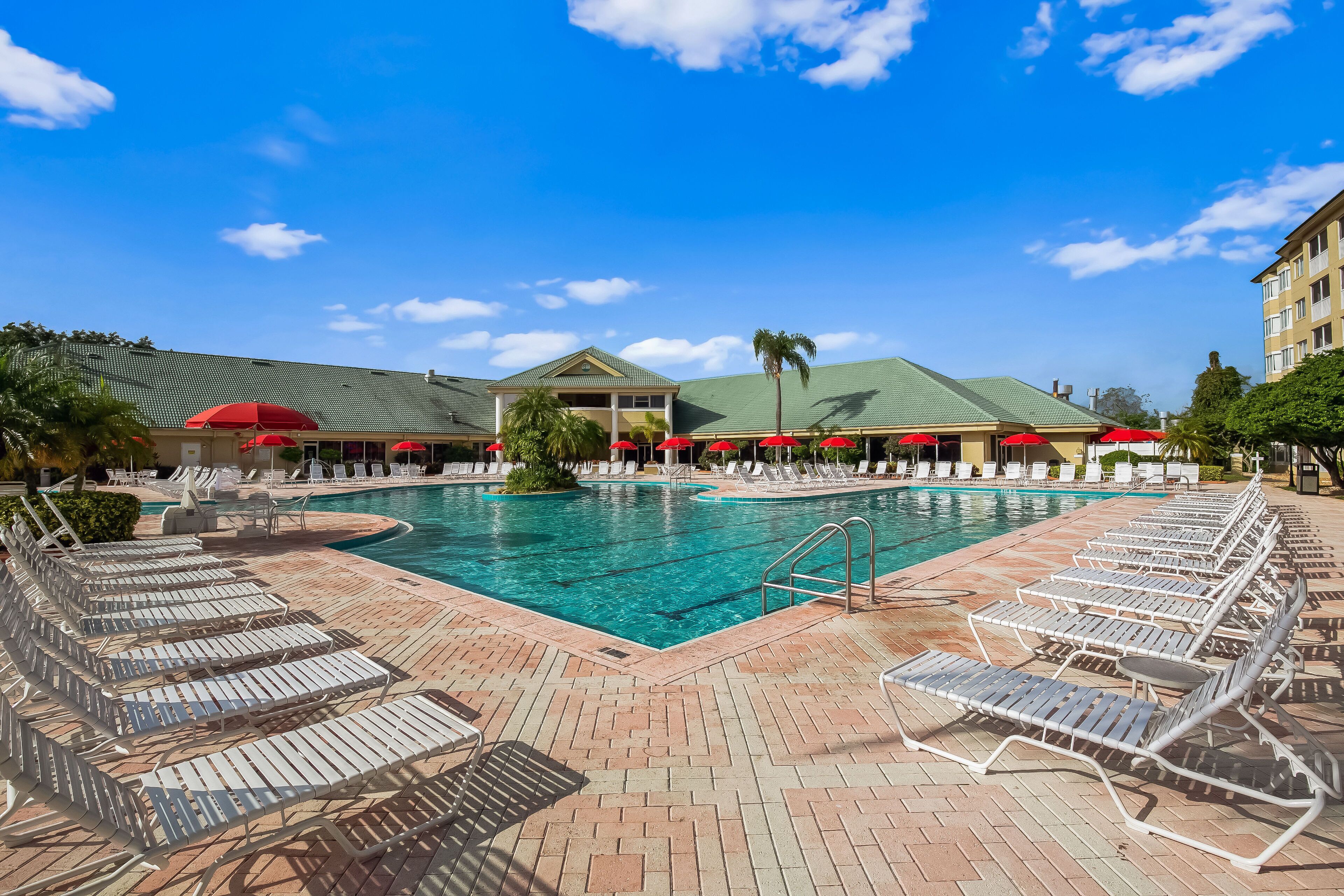 A poolside area with lounge chairs and umbrellas, a clear blue sky, and a building with a green roof in the background.