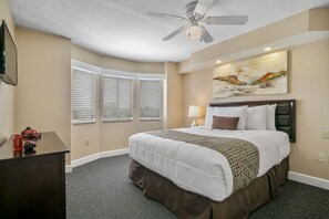 Une chambre d’hôtel avec un grand lit, un ventilateur de plafond, un tableau au mur et un bureau avec une lampe.