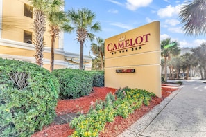 A sign for Camelot by the Sea with a 'VACANCY' sign below it, surrounded by landscaped gardens and palm trees.