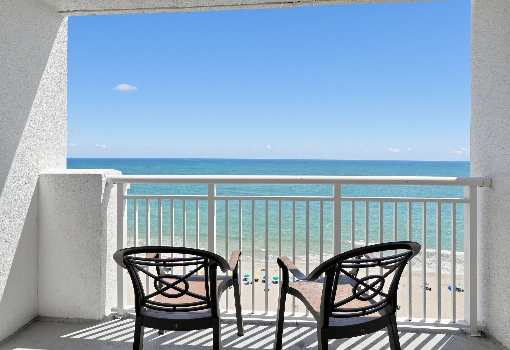 A balcony with two chairs facing a beach.