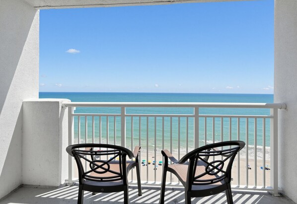 A balcony with two chairs facing a beach.