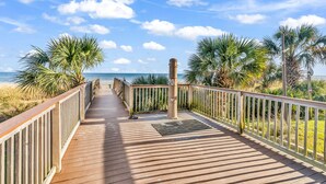 A wooden boardwalk leading to the beach with palm trees and a clear sky.