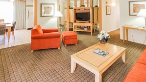 Hotelkamer met een bank, voetenbankje, salontafel, televisie en een eethoek met stoelen en een tafel.