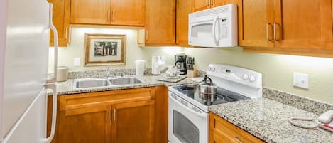 Kitchen with wooden cabinets, double sink, stove, and microwave