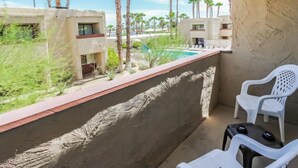 Een balkon met witte plastic stoelen, een zwembadje en palmbomen op de achtergrond.
