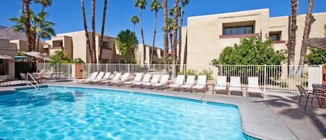 Una piscina con sillas de descanso, palmeras y un edificio con balcones.