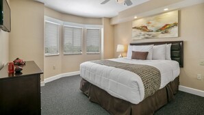 A hotel room with a large bed, a ceiling fan, a painting on the wall, and a desk with a lamp. - Spacious 2BR Condo near Disney (Kissimmee)
