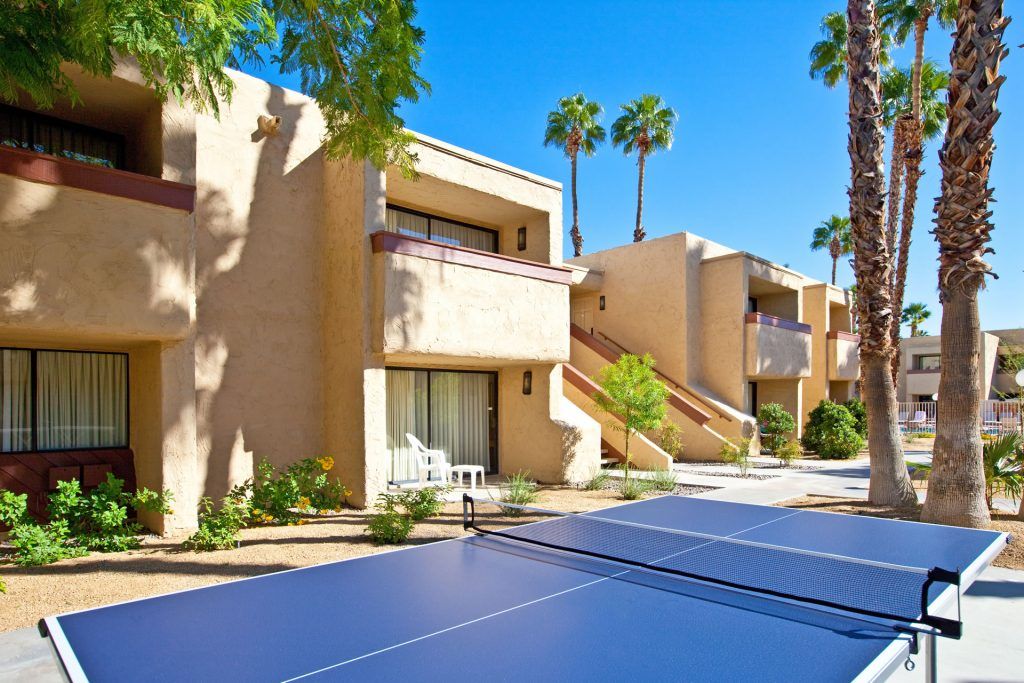Una cancha de tenis junto a un edificio con balcones y palmeras.