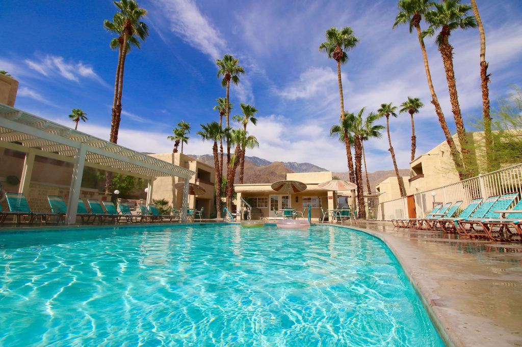 A swimming pool with lounge chairs, palm trees, and a building in the background.