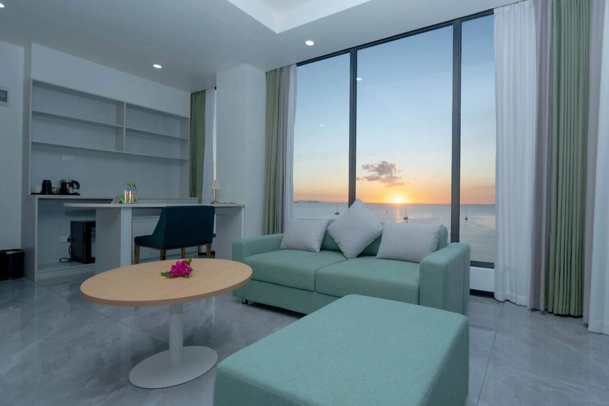 A modern living room with a sofa, a round table, and a view of the sunset over the sea.