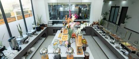 A buffet setup with various food stations, including a coffee bar, and a large window providing a view of the outside.