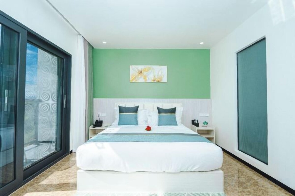 A modern bedroom with a large bed, a nightstand, a bedside table, and a window with a view.