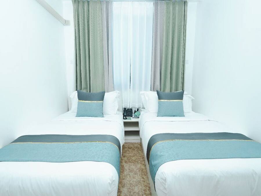 Una habitación de hotel con dos camas, una mesita y un ventanal con cortinas.