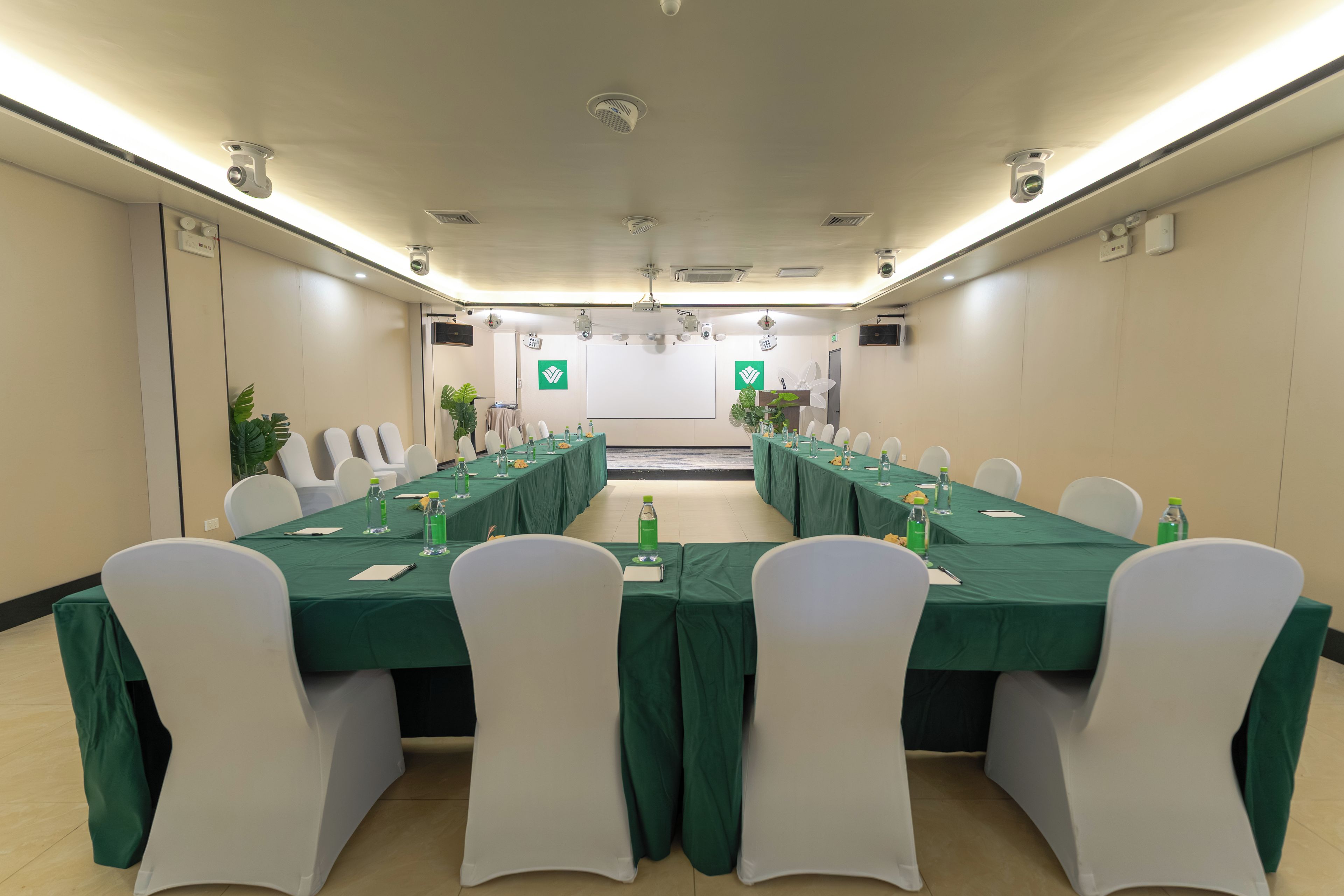 Un salón de conferencias con una mesa larga, sillas blancas y manteles verdes.
