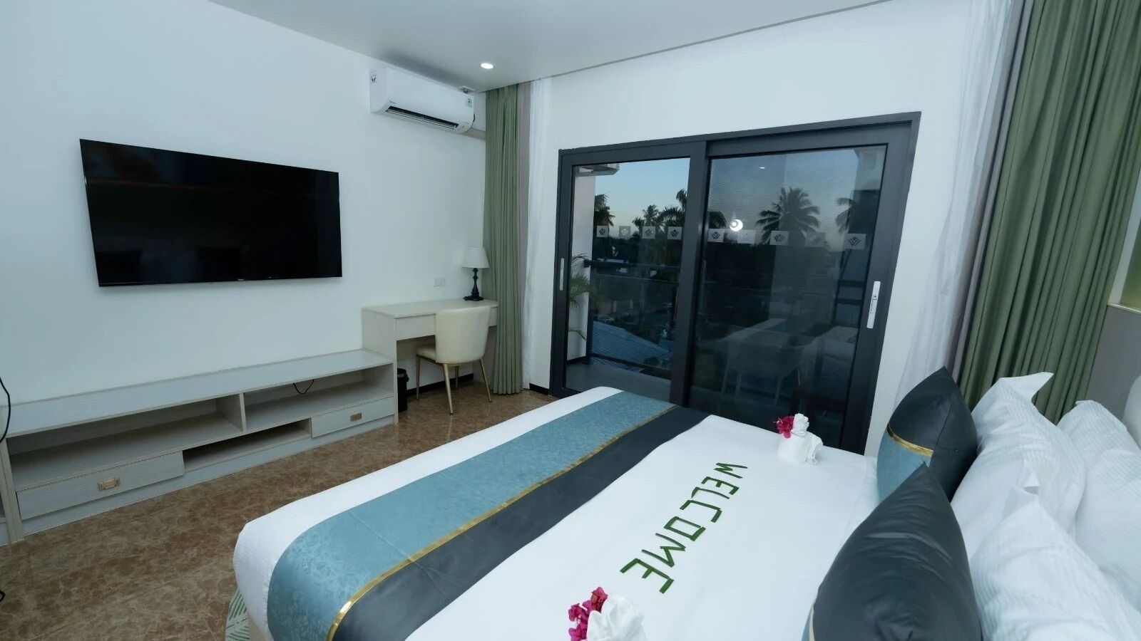 A hotel room with a bed, a desk, a TV, and a sliding glass door to the outside.