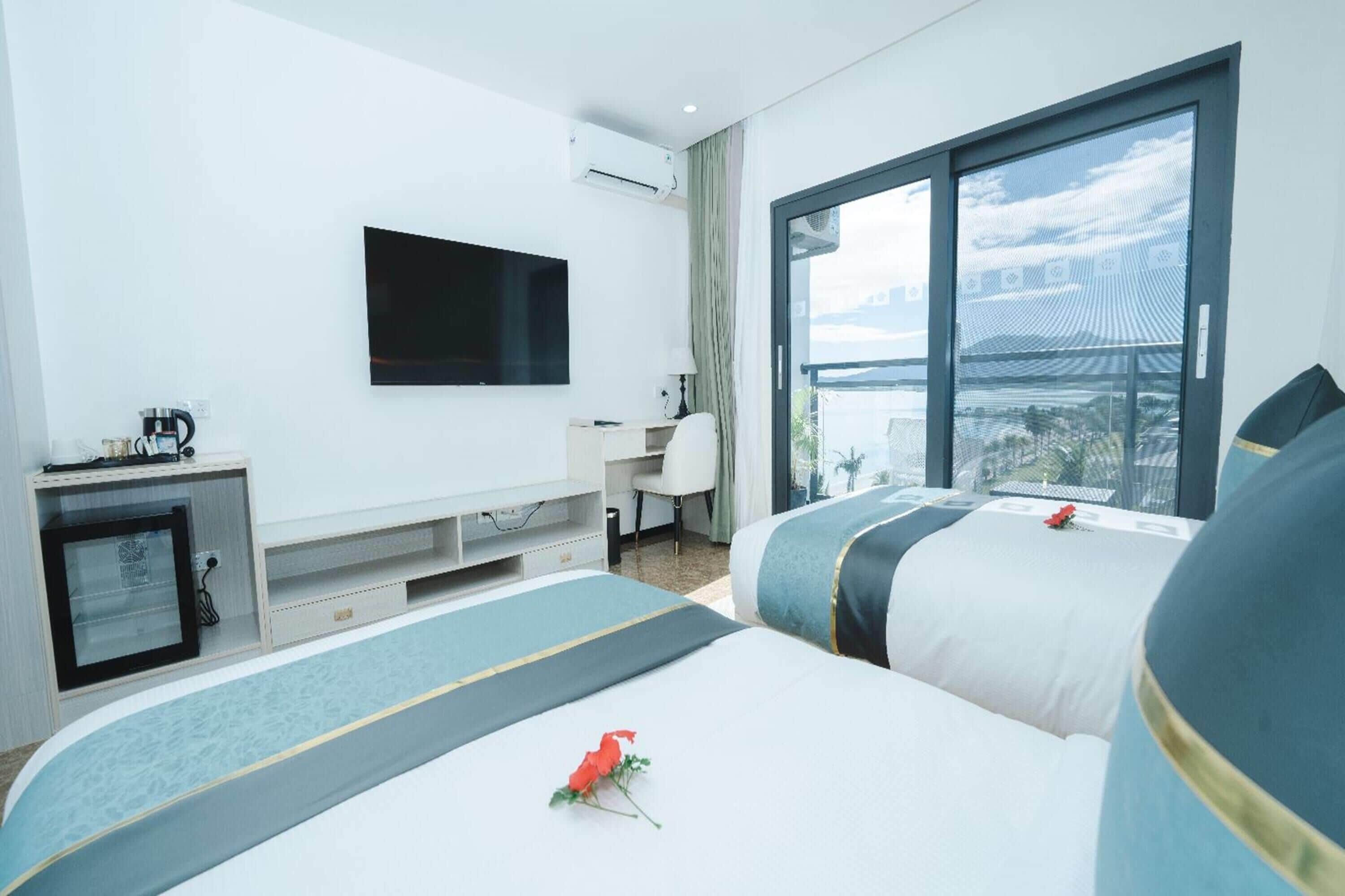 A hotel room with two beds, a desk, a TV, and a large window with a view.