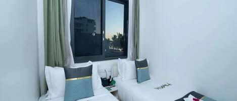 A hotel room with two beds, a window with curtains, and a view of palm trees.