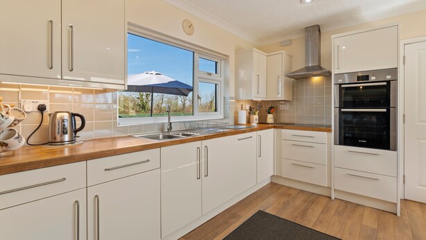 A modern kitchen with white cabinets, stainless steel appliances, and a window with an umbrella.