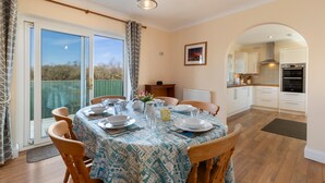 A dining area with a table set for four, a kitchen in the background, and a view through the glass door.