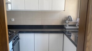 A compact kitchen with white cabinets, a black countertop, and a dish rack.