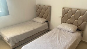 Two single beds with tufted headboards in a room with plain walls and a tiled floor.
