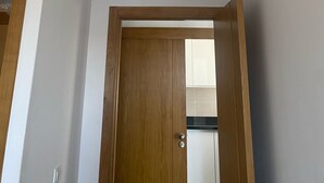 A room with a wooden door, white walls, and a ceiling vent.