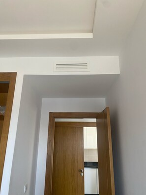 A room with a wooden door, white walls, and a ceiling vent.