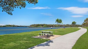 Een park aan het meer met een wandelpad, picknicktafels en mensen die aan het vissen zijn.