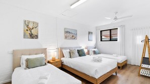 Een hotelkamer met drie bedden, een houten vloer, witte muren en kunstwerken.
