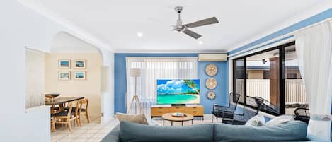 Ein Wohnzimmer mit Sofa, Fernseher, Essbereich und Deckenventilator.